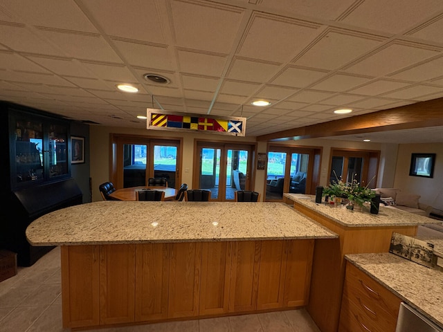 169 Pine Bluffs Rd, Roscommon, MI 48653 - kitchen featuring light tile patterned flooring, light stone countertops, brown cabinetry, open floor plan, and a kitchen island