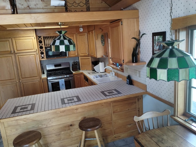 19241 Pine Tree Ct, Hillman, MI 49746 - kitchen featuring stainless steel gas range, wallpapered walls, tile countertops, a breakfast bar area, and a peninsula