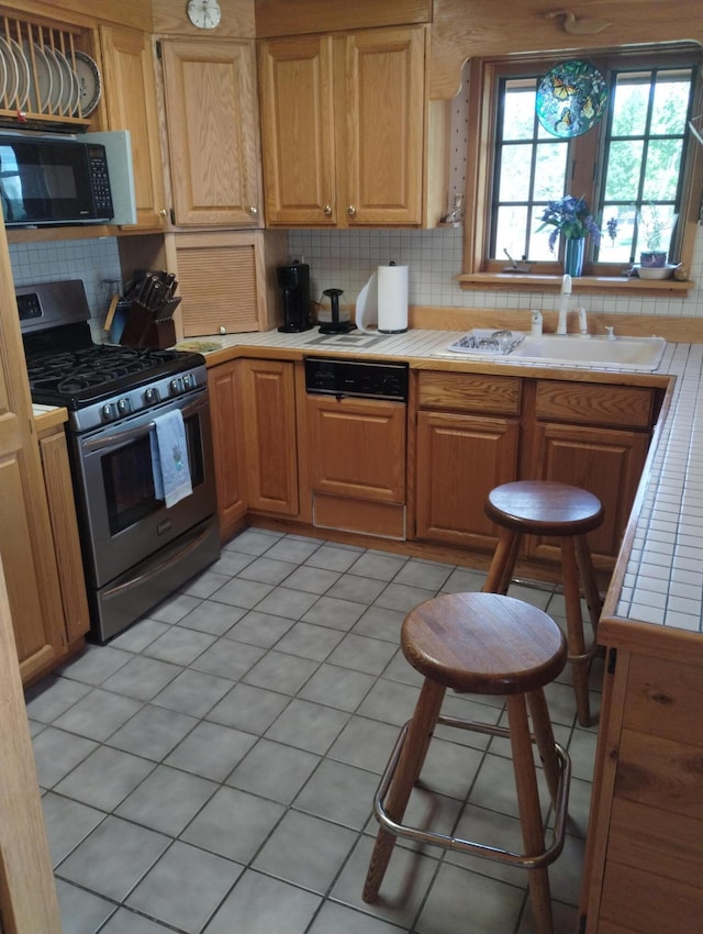 19241 Pine Tree Ct, Hillman, MI 49746 - kitchen featuring black microwave, gas range, tile countertops, tasteful backsplash, and light tile patterned flooring