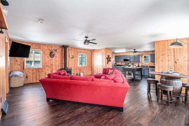 2145 Mustang St, Saint Helen, MI 48656 - living room featuring ceiling fan, a wood stove, wood walls, and dark wood finished floors