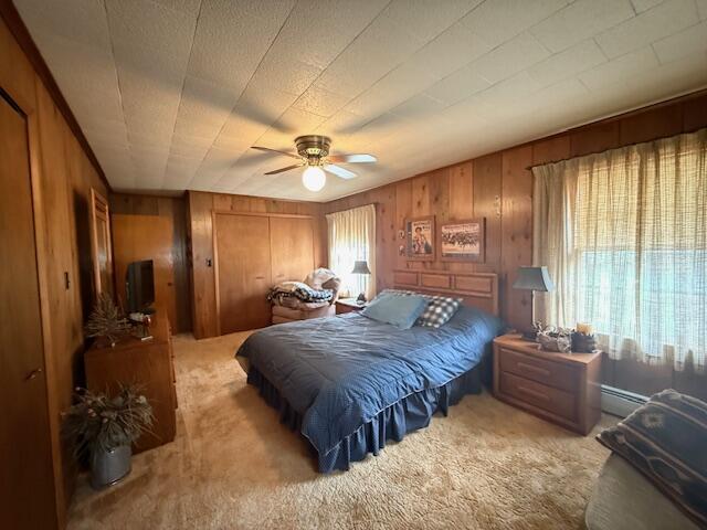 119 Ethel Dr, Roscommon, MI 48653 - carpeted bedroom with wood walls, a closet, ceiling fan, and a baseboard radiator