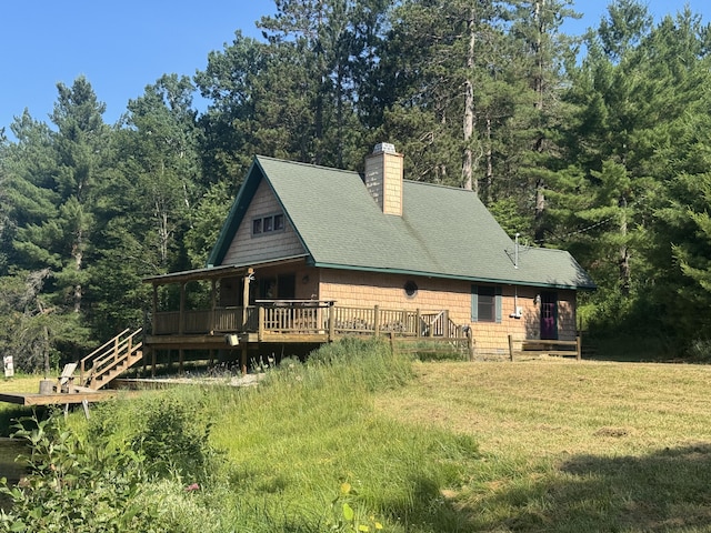 5283 Griffin Rd, Lewiston, MI 49756 - view of side of property with a chimney, a wooden deck, a yard, roof with shingles, and a wooded view