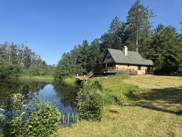 5283 Griffin Rd, Lewiston, MI 49756 - view of home's exterior featuring a view of trees, a chimney, a deck with water view, and a lawn