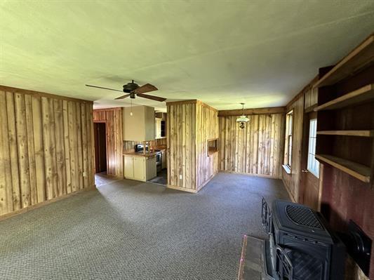 605 N Poor Farm Rd, Harrisville, MI 48740 - unfurnished living room with wood walls, a ceiling fan, and carpet