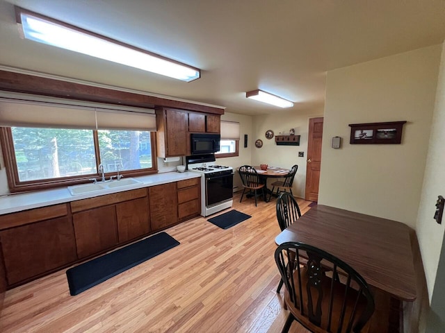 332 Pingree St, Roscommon, MI 48653 - kitchen with black microwave, white range with gas cooktop, light wood-type flooring, light countertops, and brown cabinetry