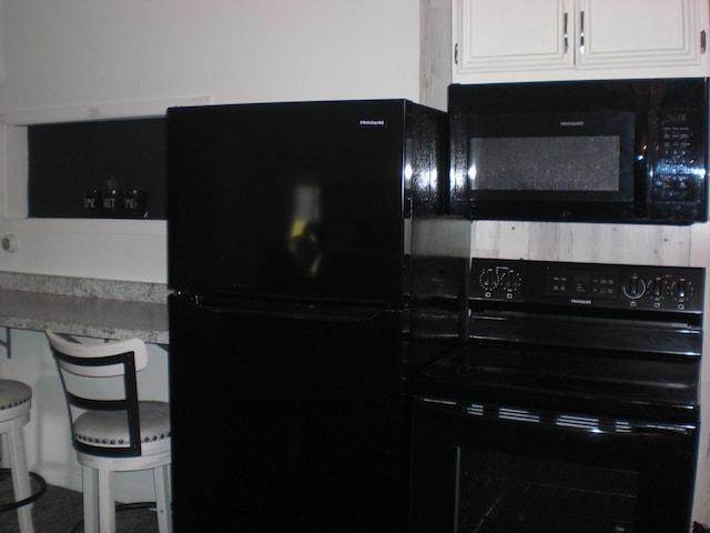 557 Davis St, Lake, MI 48632 - kitchen featuring black appliances, white cabinets, a breakfast bar, and light countertops