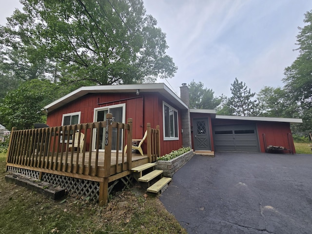 1300 Geesey Ave, Mio, MI 48647 - view of front of home featuring a chimney, asphalt driveway, a garage, board and batten siding, and a deck