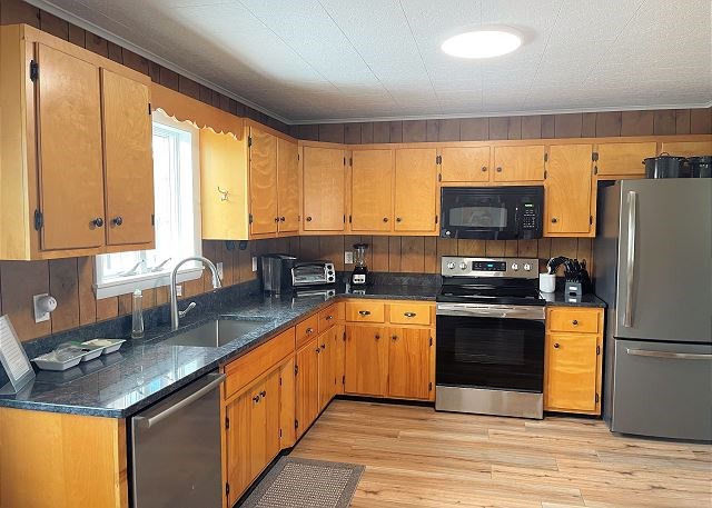 kitchen featuring sink, wooden walls, stainless steel appliances, and light wood-type flooring