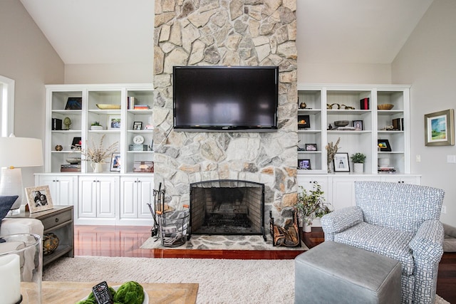 living room featuring hardwood / wood-style flooring, a stone fireplace, and vaulted ceiling