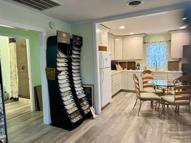 kitchen featuring white refrigerator, light wood-type flooring, white cabinetry, and sink