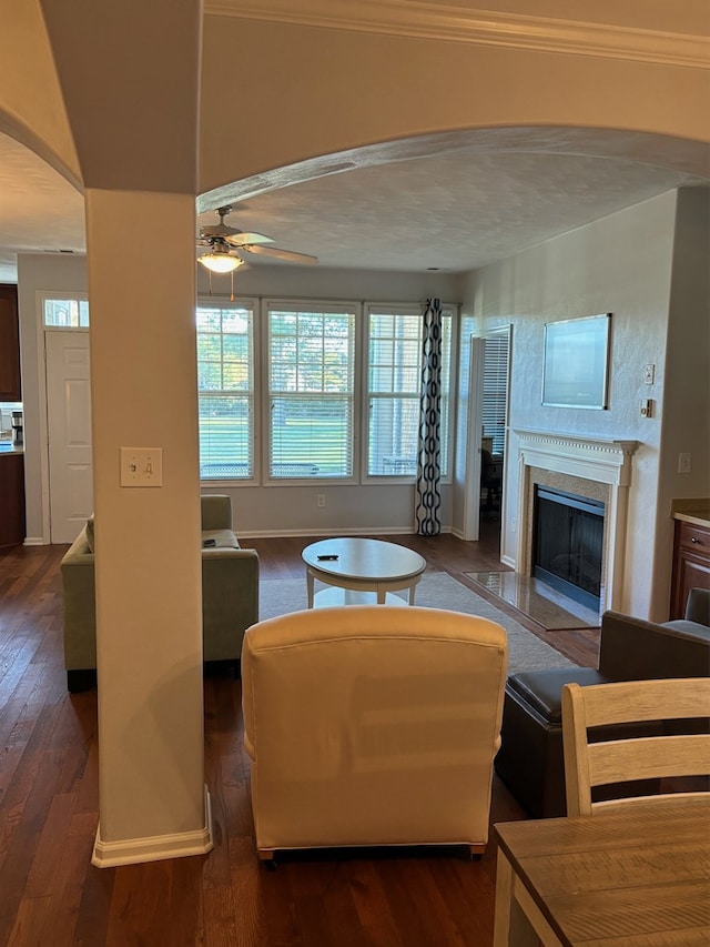 living room with dark wood-type flooring, ornamental molding, and ceiling fan