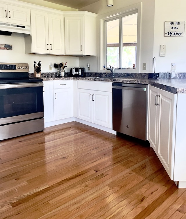 kitchen with appliances with stainless steel finishes, range hood, white cabinetry, sink, and light hardwood / wood-style floors