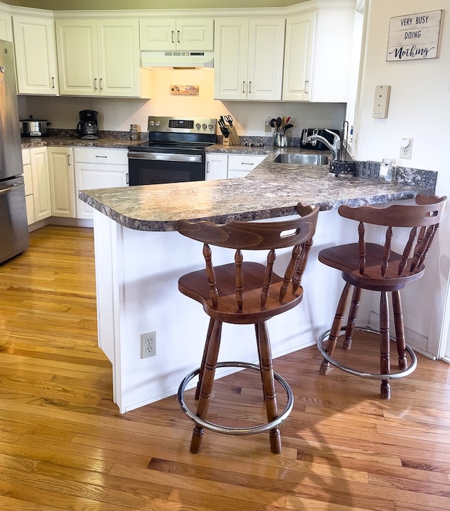 kitchen featuring sink, appliances with stainless steel finishes, white cabinets, a kitchen bar, and kitchen peninsula