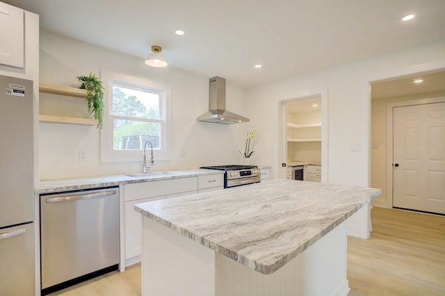 kitchen with wall chimney exhaust hood, light wood finished floors, white cabinets, a sink, and appliances with stainless steel finishes