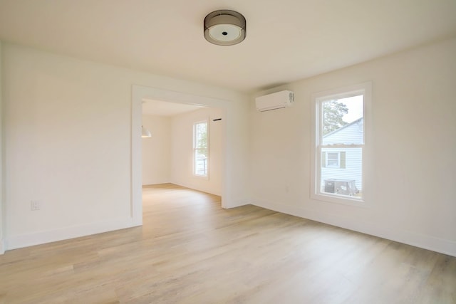 spare room featuring light wood finished floors, baseboards, and an AC wall unit
