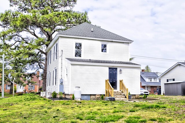back of property with a yard, a shingled roof, and entry steps