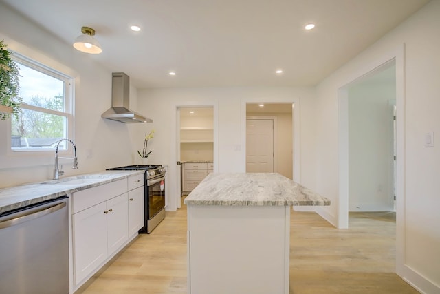 kitchen featuring wall chimney exhaust hood, white cabinetry, a center island, a sink, and stainless steel appliances