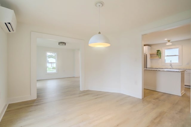 unfurnished dining area with baseboards, light wood-style floors, and a wall mounted air conditioner