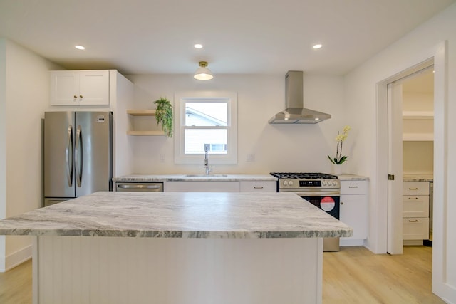 kitchen featuring wall chimney range hood, a sink, light wood-type flooring, stainless steel appliances, and white cabinetry