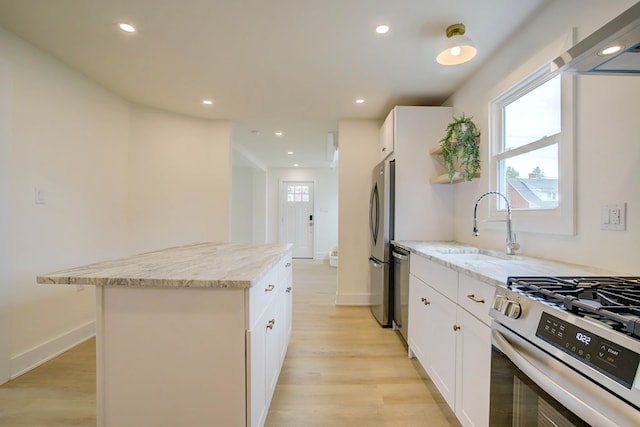 kitchen with stainless steel appliances, light wood-style flooring, a sink, light stone counters, and a kitchen island