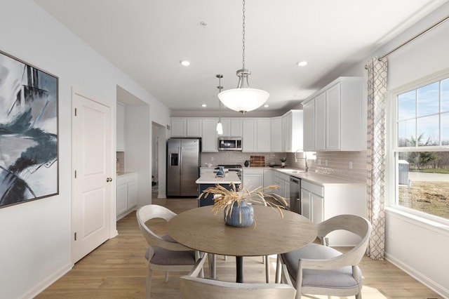 kitchen featuring white cabinetry, light wood-type flooring, decorative light fixtures, and appliances with stainless steel finishes