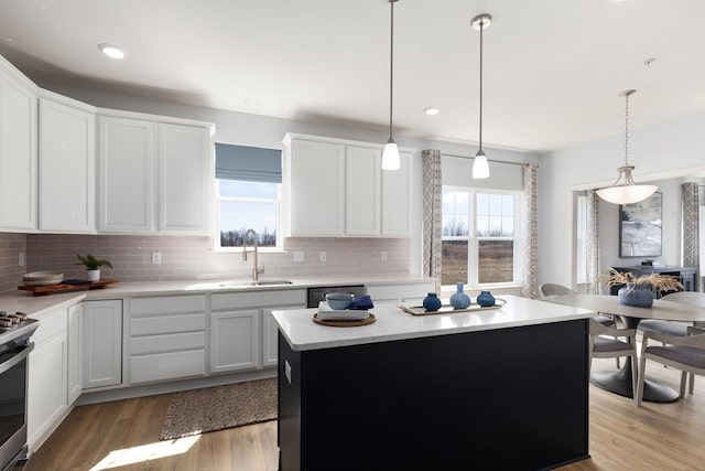 kitchen with light wood-type flooring, sink, white cabinets, a center island, and hanging light fixtures