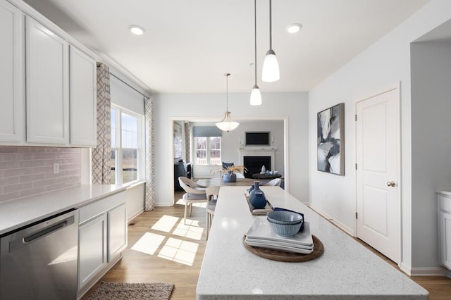 kitchen featuring decorative light fixtures, backsplash, white cabinetry, and stainless steel dishwasher