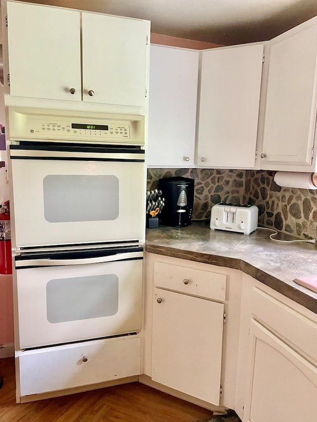 3250 Colona St, Chincoteague, VA 23336 - kitchen with white double oven, tasteful backsplash, white cabinets, dark countertops, and wood finished floors