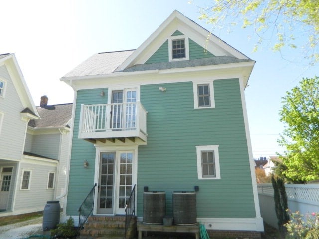 rear view of house with entry steps, a balcony, fence, and central AC