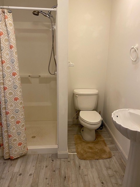 bathroom with a shower stall, toilet, baseboards, and wood finished floors