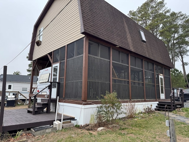 view of home's exterior featuring a wooden deck, a shingled roof, and a sunroom