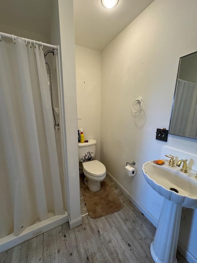 bathroom featuring toilet, a stall shower, a sink, wood finished floors, and baseboards