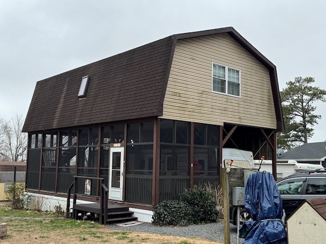 view of front of house featuring a gambrel roof, a sunroom, and a shingled roof