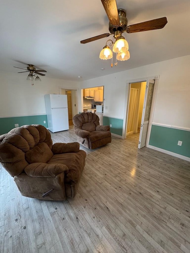 living area with baseboards, a ceiling fan, and light wood finished floors