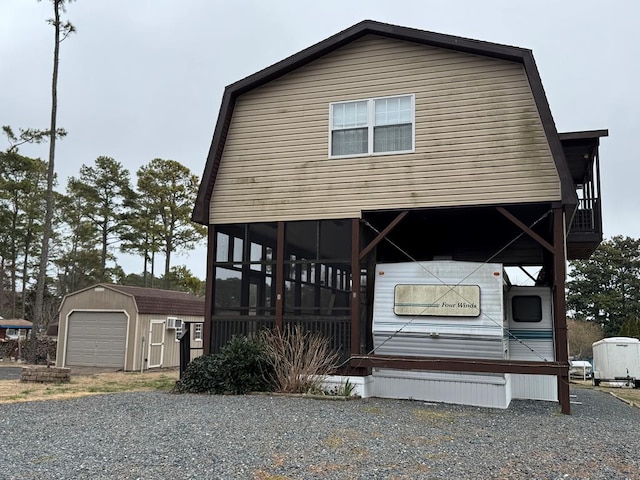 view of front of property featuring a gambrel roof, a sunroom, a garage, an outdoor structure, and driveway