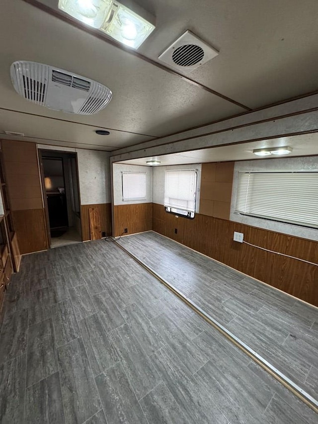 empty room featuring a wainscoted wall, wood finished floors, visible vents, and wood walls