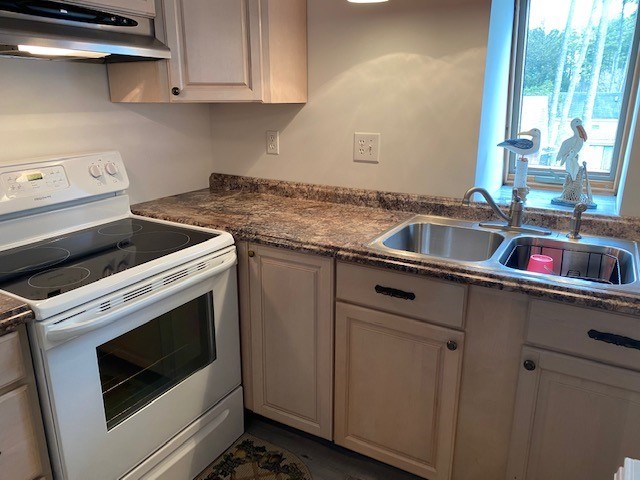 kitchen featuring under cabinet range hood, dark countertops, a sink, and white range with electric stovetop