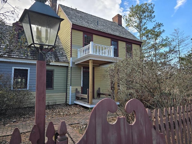 rear view of house with a balcony, a chimney, and fence