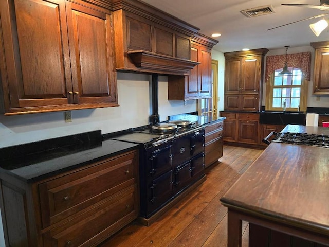 kitchen featuring visible vents, dark wood finished floors, dark countertops, ceiling fan, and a sink