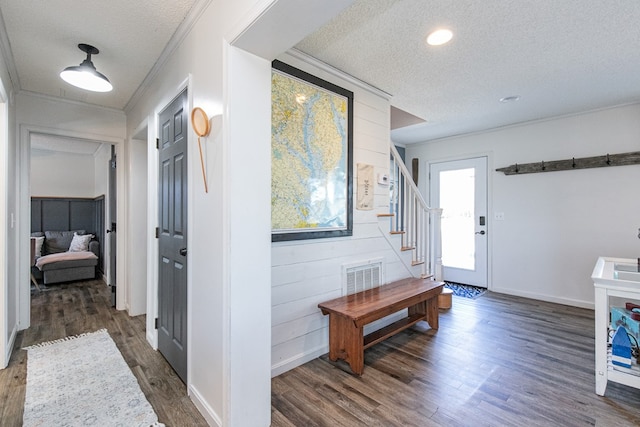 foyer featuring wood walls, dark wood-type flooring, a textured ceiling, and ornamental molding