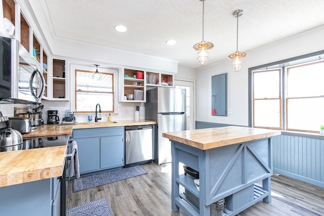 kitchen with appliances with stainless steel finishes, a textured ceiling, blue cabinetry, pendant lighting, and butcher block countertops