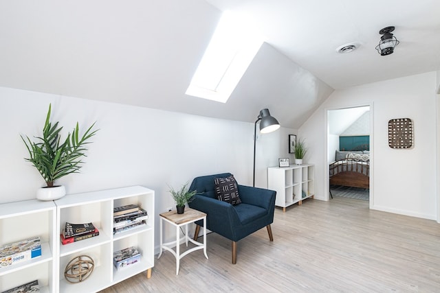 living area featuring vaulted ceiling with skylight and light hardwood / wood-style floors