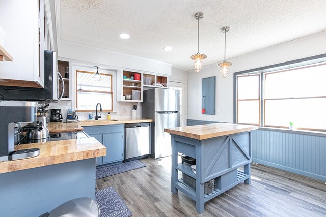 kitchen with wood counters, blue cabinets, hanging light fixtures, a textured ceiling, and appliances with stainless steel finishes