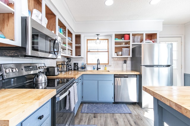 kitchen featuring appliances with stainless steel finishes, a textured ceiling, sink, blue cabinetry, and butcher block countertops