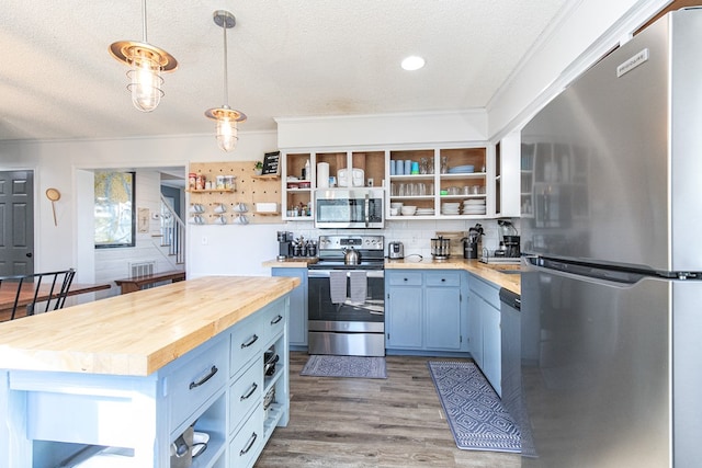 kitchen featuring a center island, blue cabinets, butcher block countertops, decorative light fixtures, and stainless steel appliances