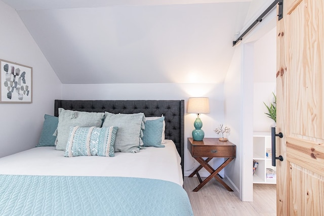 bedroom with wood-type flooring, a barn door, and vaulted ceiling