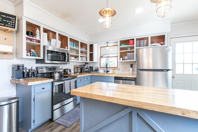 kitchen with wood counters, a textured ceiling, stainless steel appliances, blue cabinets, and pendant lighting