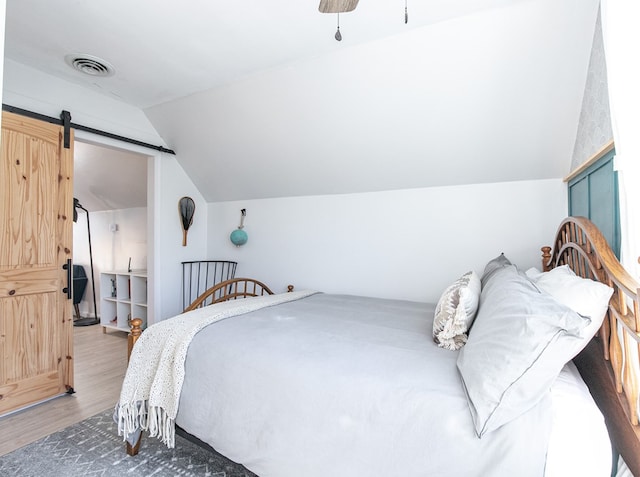 bedroom featuring hardwood / wood-style floors, a barn door, ceiling fan, and lofted ceiling