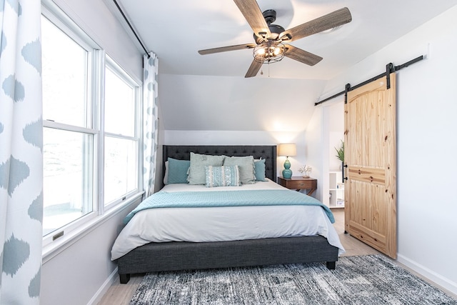 bedroom with ceiling fan, a barn door, wood-type flooring, and lofted ceiling