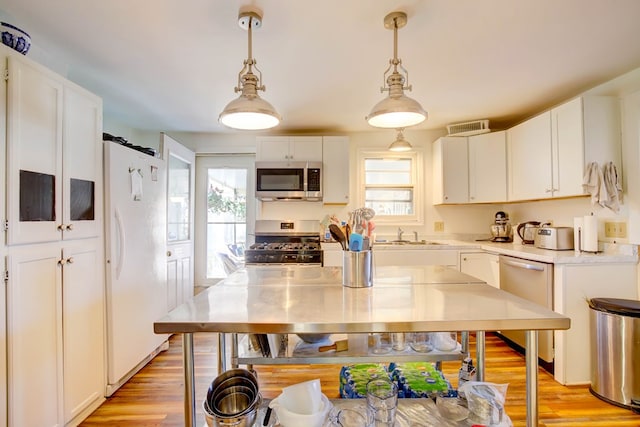 kitchen featuring light wood-type flooring, white cabinetry, hanging light fixtures, and appliances with stainless steel finishes